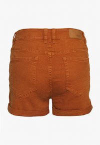 Vista trasera de pantalones cortos de mezclilla color naranja quemado con dobladillos enrollados, dos bolsillos traseros, passadores para cinturón y un pequeño parche de cuero de la marca en la cinturilla.