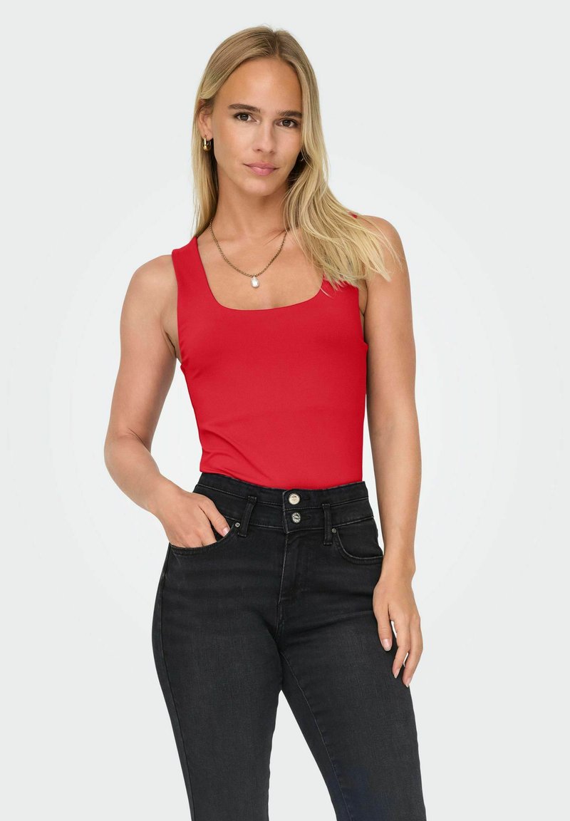 Rode mouwloze body met een vierkante halslijn, gecombineerd met hoge zwarte jeans. De ensemble heeft een gladde, aansluitende textuur.