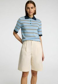 Randig pikétröja i ljusblått med marinblå krage och manschetter, kombinerad med högmidjade beiga shorts med veck och sidofickor.