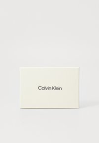 Boîte rectangulaire blanche avec une texture lisse ; présente "Calvin Klein" imprimé en noir dans une police sans-serif à l'avant.