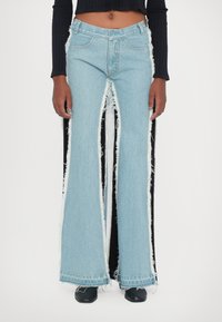 Jeans acampanados de azul claro con bordes desgastados, aberturas laterales y acentos negros en los costados. Hechos de denim con un acabado texturizado.