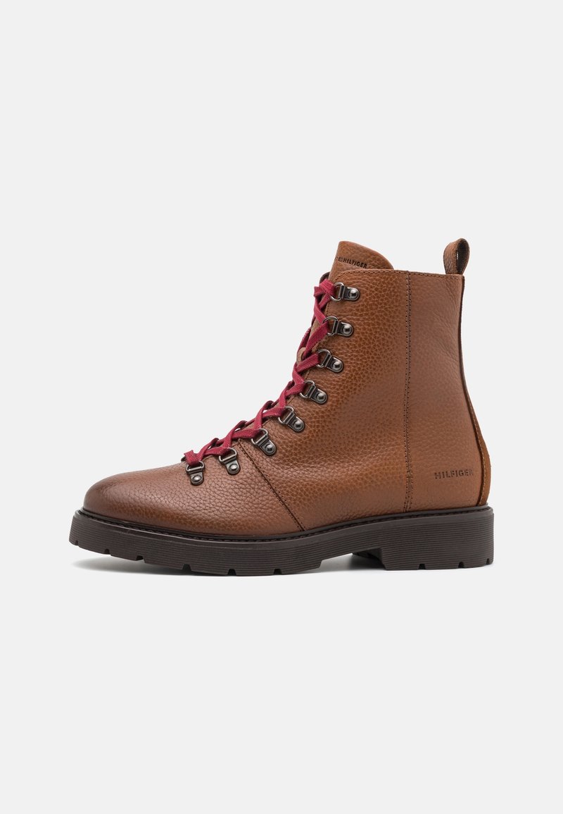 Botas de senderismo de cuero marrón con acabado texturizado, que cuentan con cordones burdeos, ojales metálicos y una suela negra resistente. Logo visible en el lado.