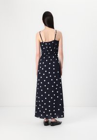 Rochie maxi bleumarin cu buline albe, având bretele subțiri și un talie elastică. Purtați cu pantofi plata negri.
