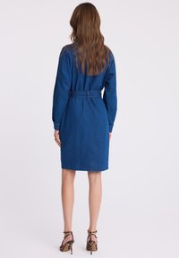 Sukienka koszulowa z denimu, z długimi rękawami, paskiem w talii i długością do kolan. Wykonana z niebieskiego materiału i o prostym kroju. Noszona z szpilkami w leopardzi wzór.