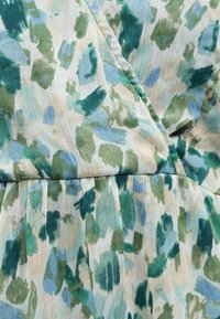 Κοντινό πλάνο ανοιχτού υφάσματος με πράσινο, μπλε και μπεζ αφηρημένο μοτίβο πινελιών και ορατές κάθετες υφασμάτινες γραμμές.