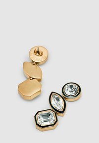 Náušnice ve zlatém tónu s geometrickými tvary a průhlednými drahokamy. Obsahují kulatou náušnici a dvě visící části s hladkým povrchem.