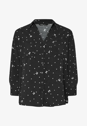 Musta nappikauluksinen paita, jossa on valkoisia pilkkuja ja pieniä rusetteja, varustettuna kauluksella ja kahdella etutaskulla. Kangas näyttää pehmeältä ja kevyeltä.