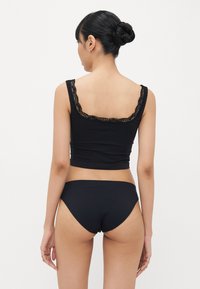 Crop top noir avec une bordure en dentelle le long de l'encolure, associé à une culotte taille haute noire assortie. Tissu lisse, design ajusté.