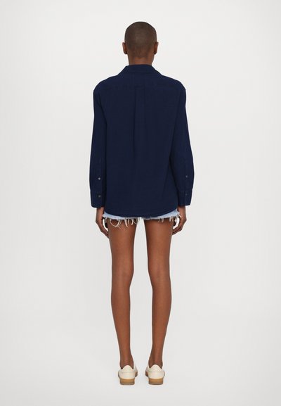 Marinskjorta med långa ärmar, lös passform, rak rygg och mjuk struktur. Matchas med denimshorts och ljusa skor.