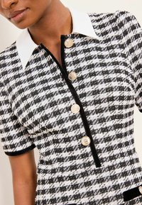 Fekete-fehér kiskockás ruha rövid ujjakkal, fehér gallérral és arany gombokkal az elején. Fekete szegélyekkel és zseb díszítésekkel.