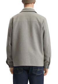 Grau gemischte Wolljacke mit Kragen und langen Ärmeln, mit einem lässigen Schnitt und sichtbaren Nähten, kombiniert mit dunklen Jeans.