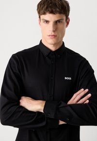 Black button-up shirt made of smooth fabric featuring a pointed collar, long sleeves, and a small white "BOSS" logo on the chest.