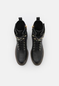 Botas de cuero negras hasta el tobillo con tachuelas de pirámide doradas, cordones en la parte delantera, cremallera lateral y costuras decorativas a lo largo de la suela.
