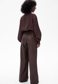 Brązowa bluzka z długim rękawem oraz wysokie, szerokie spodnie z faux leather. Gładka tekstura, luźny krój, marszczony pasek w talii oraz bogaty kolor.