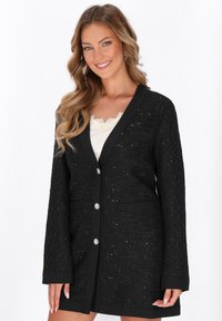 Blazer nero con texture, scollo a V, maniche lunghe, due tasche e bottoni decorativi. Presenta un motivo intrecciato e rifiniture a contrasto.