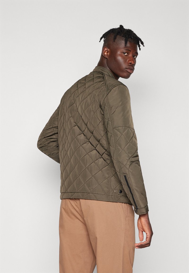 Olivgrüne gesteppte Jacke mit hohem Kragen, seitlichen Reißverschlüssen und taillierter Passform. Der Stoff hat eine glatte Textur und einen matten Glanz.