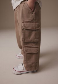 Beige cargobroek van katoen met twee grote zijzakken, een losse pasvorm en een opgerolde zoom, gecombineerd met witte sneakers met bandjes.