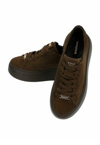 Sneaker in suede marrone con suola piatta scura, dotate di lacci e un accento metallico su un lato, progettate per un uso casual.