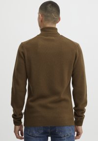 Pull en tricot marron avec un col haut, des poignets et un ourlet côtelés. Le tissu semble doux avec une finition texturée. Porté sur un jean bleu.