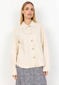 Light beige button-up jacket with a collar, two front pockets, and silver buttons. Long sleeves with a relaxed fit and minimal stitching details.