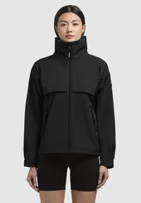 Giacca nera impermeabile con colletto alto, zip frontale e grande tasca sul petto. Presenta due tasche laterali con zip e dettagli ai polsini.
