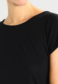 Czarny bawełniany T-shirt z szerokim dekoltem, krótkimi rękawami i gładką, lekką fakturą. Widoczny detal szewkowy w pobliżu dołu.