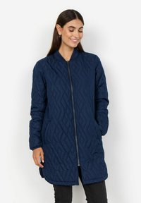 Mörkblå quiltad lång jacka med zippered front, ribbad krage och diamantmönster. Har långa ärmar och sidofickor.