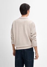 Pull en maille beige avec un ourlet et des manches côtelés, doté d'un col classique. Associé à un pantalon en denim bleu foncé, présentant peu de détails de design.
