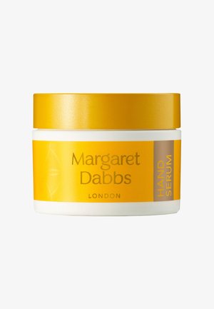 Pot jaune et blanc de sérum pour les mains. Présente un couvercle doré, une étiquette transparente avec le texte "Margaret Dabbs London" et "SÉRUM POUR LES MAINS" en marron.