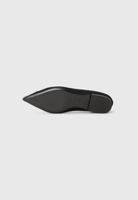 Chaussure en suède noir à bout pointu avec un design élégant et un talon bas et effilé. La semelle est lisse et légèrement texturée pour une meilleure adhérence.