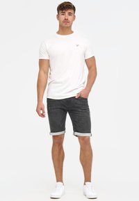 T-shirt blanc à manches courtes pour hommes avec un petit logo, associé à un short en denim foncé retroussé aux ourlets et des baskets blanches. Design simple, coupe décontractée.