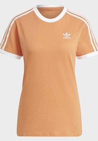 Orange bomullströja med vita detaljer på den runda halsringningen och ärmkanterna. Har tre vita ränder på axlarna och en logotyp.