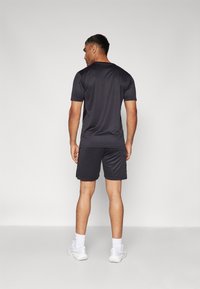 Donkere grijze sportshirt en shorts van lichtgewicht, ademend materiaal. Heeft korte mouwen, een ronde hals en een aansluitende pasvorm.