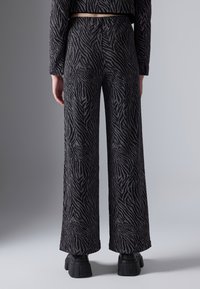 Wijd-benige broeken in een zwart-zilver kleurige zebraprint. Gemaakt van een gestructureerde stof met een getailleerde pasvorm en een elastische tailleband.
