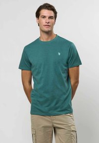 Mėlynos spalvos trumpomis rankovėmis marškiniai, pagaminti iš minkštos, tekstūruotos medžiagos, su apvaliu iškirpimu. Ant kairiojo krūtinės šono yra mažas logotipas.