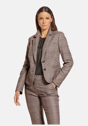 Bruin geruit pak bestaande uit een getailleerde blazer met twee knopen en bijpassende, smalle broek, gecombineerd met een zwarte blouse. Gladde textuur.