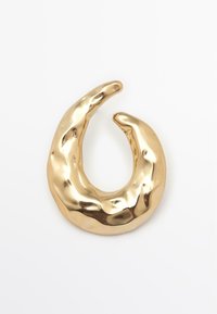 Brož zlaté barvy s abstraktním tvarem, hladkým a leštěným povrchem, se zkrouceným organickým tvarem a jemnými prohlubněmi pro texturu.