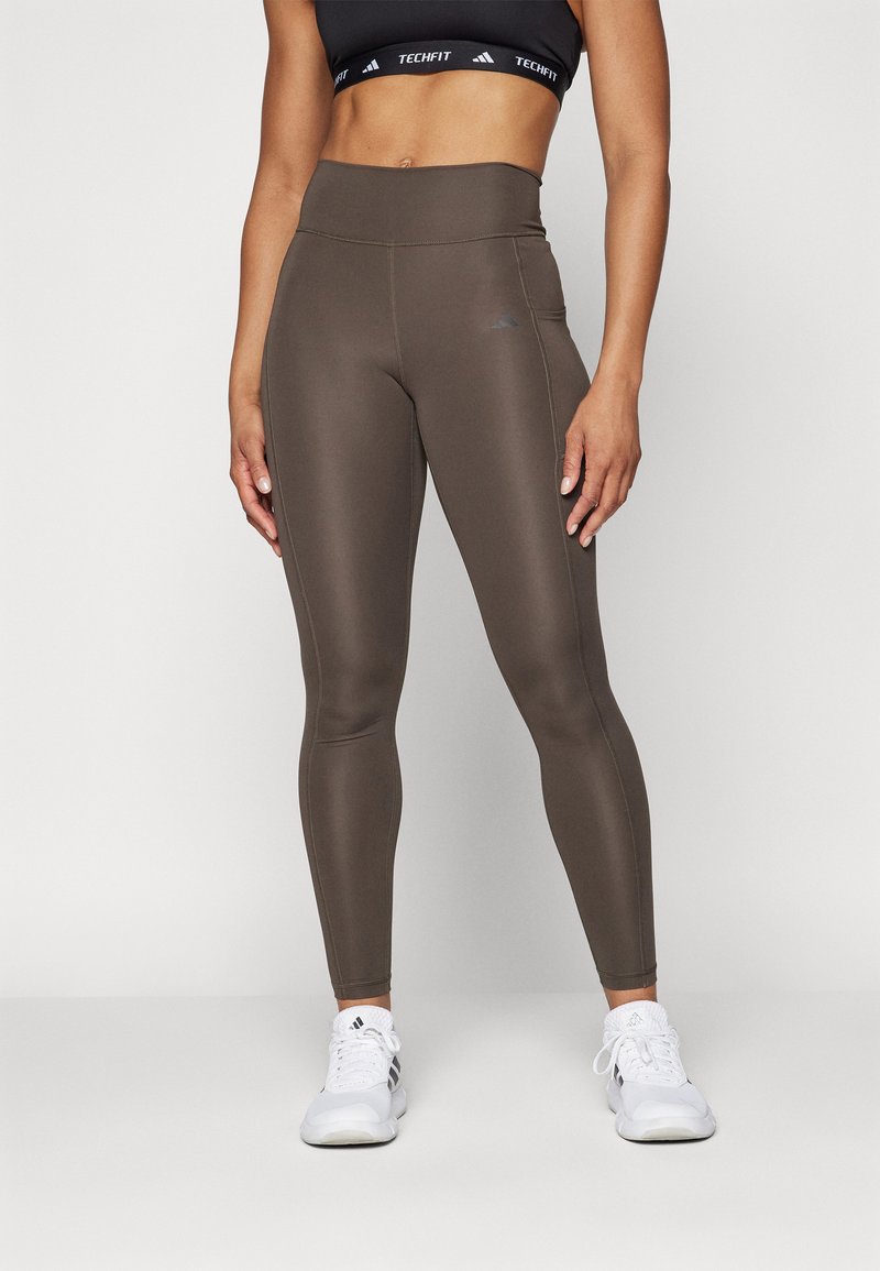 High-waisted, form-fitting leggings in dark brown, made from a smooth, stretchy fabric; features discreet side pocket and contrasting stitching.