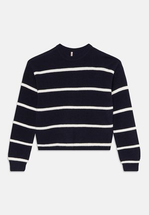 Tumši zils džemperis ar baltām horizontālām svītrām. Ar ribotu faktūru un apaļu kakla izgriezumu. Garas piedurknes, īsa piegriezuma. Nav redzamu piederumu.