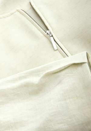 Close-up of a partially open silver zipper on textured off-white fabric with a folded section.