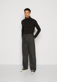 Svart langermet turtleneck kombinert med grå stripete vide bukser og svarte sneakers, som viser en jevn bomullstekstur og tilpasset passform.