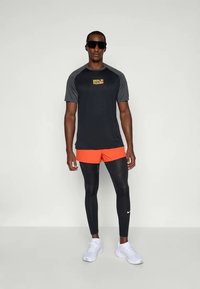 Svart og grå kortermet løpet skjorte med teksten "BERLIN RUN"; oransje shorts; svarte leggings med Nike-logo; hvite treningssko; solbriller.