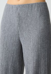 Grijze ribgebreide broek met een hoge tailleband. De textuur is zacht en opvallend, met verticale strepen die de lengte van de stof volgen.