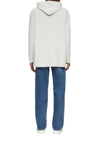 Oversized biały hoodie z kapturem na sznurek, połączony z luźnymi niebieskimi dżinsami. Gładka tekstura materiału, swobodny design, minimalne zdobienia.
