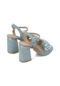 Sandali con tacco alto in suede di colore blu chiaro, con un tacco spesso accentuato in argento e una parte anteriore decorata con grandi gemme trasparenti. Cinturino regolabile.