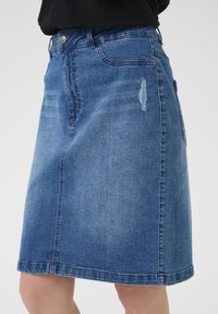 Denimskørt i mellemblå med lige snit, prydet med en sølvknap og slidte detaljer foran, knælang længde.