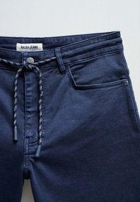 Jeans de mezclilla azul marino con cintura elástica y cordón ajustable, costuras sutiles y un único bolsillo frontal. La etiqueta dice "SALSA JEANS".