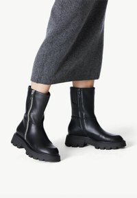 Black leather ankle boots with a chunky sole, zipper detail on one side, and a smooth texture. Similar height and design on both boots.