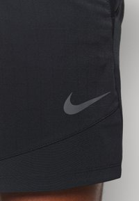 Nike shorts in black, featuring a textured grid pattern, an embroidered gray logo on the lower leg, and neat stitching along the seams.