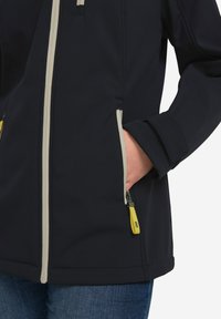 Veste softshell marine avec fermeture éclair gris clair, tirette de fermeture éclair jaune contrastante et poches latérales. Texture lisse et design ajusté.